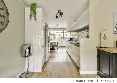 A stylish minimalist kitchen featuring sleek cabinetry, wooden flooring, and elegant plants. The layout emphasizes functionality and modern design aesthetics. A stylish minimalist kitchen featuring sleek cabinetry, wooden flooring, and elegant plants. The layout emphasizes functionality and modern design aesthetics. 123834084