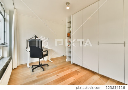A sleek and contemporary home office setup featuring a minimalist desk, chair, and storage units crafted in a light color scheme on wooden flooring. 123834116
