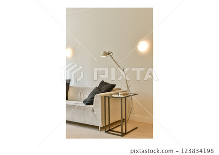 A sleek modern living room featuring a cozy sofa adorned with cushions and a contemporary floor lamp beside a stylish glass side table. 123834198