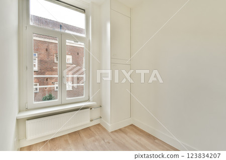 A clean and bright interior space featuring a large window that allows natural light to flood in. The simplicity and minimalism highlight modern design. A clean and bright interior space featuring a large window that allows natural light to flood in. The simplicity and minimalism highlight modern design. 123834207