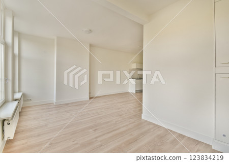 A spacious, minimalist interior with light-colored walls and wooden flooring, highlighting simplicity and elegance in home design. 123834219