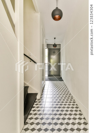 A stylish interior hallway featuring a blend of geometric tiled flooring and contemporary lighting. The staircase complements the minimalist aesthetic. A stylish interior hallway featuring a blend of geometric tiled flooring and contemporary lighting. The staircase complements the minimalist aesthetic. 123834304