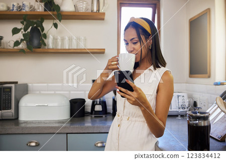 Drinking coffee, phone and black woman in a home kitchen on a relax morning using technology. Mobile, texting and social media app scroll of a person from Spain in a house watching a web video 123834412