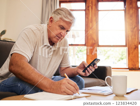 Smartphone, budget planning and senior man in living room for retirement research, website investment information or asset management. Elderly person writing notes, using phone online finance banking 123834420