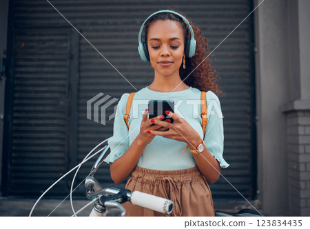 Music, bicycle and girl on her phone in the city with headphones on. Technology, summer fashion and young woman on her smartphone streaming song, track and radio online and cycling bike in urban town 123834435