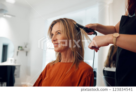 Hairdresser, flat iron and woman in salon for hair appointment with happy customer. Stylist using hair straightener on client in beauty salon or hair shop for straight hair, heat treatment and style 123834541