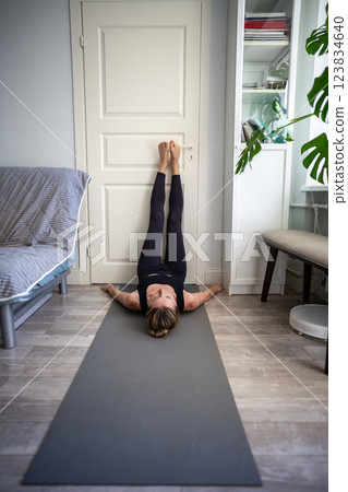Woman with closed eyes, meditating on mat with feet against door and arms stretched on floor Woman with closed eyes, meditating on mat with feet against door and arms stretched on floor 123834640