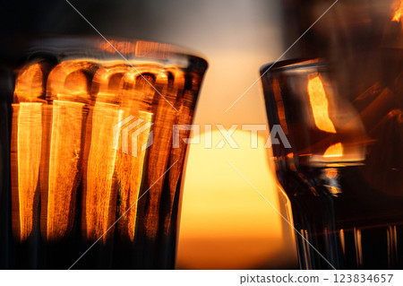 Closeup of wine glass, faceted tumbler, goblet, shot glass for drinks illuminated by orange light.  123834657