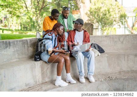 Focused African American students friends on park bench engaged with laptop. Working on assignment 123834662