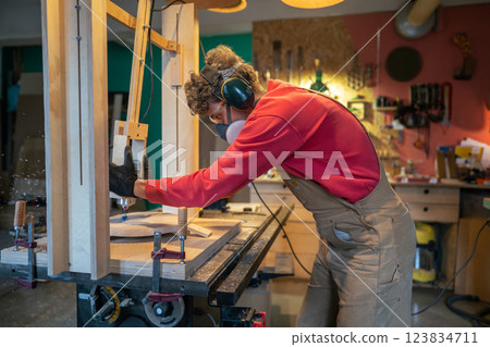 Carpenter in protective gear sands stool foundation in wood workshop. Smooth finishing, sculpting Carpenter in protective gear sands stool foundation in wood workshop. Smooth finishing, sculpting 123834711