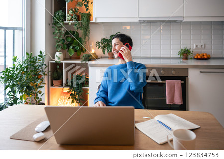 Remote boss. Smiling woman managing freelance projects with phone call and laptop in home office Remote boss. Smiling woman managing freelance projects with phone call and laptop in home office 123834753