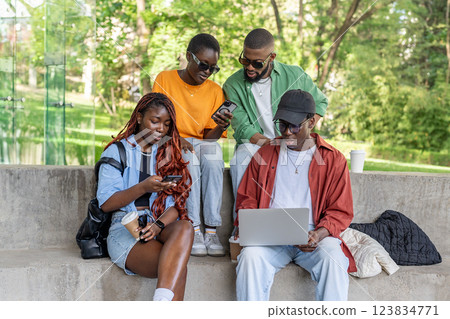 Group of interracial friends on bench work on laptops, phones. Digital native students exploring Net 123834771