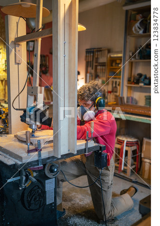Man woodworker in protective gear shaping stool base on drilling cnc machine in furniture workshop 123834778