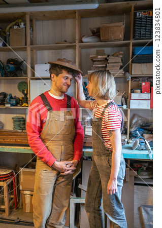 Playful couple of carpenters in workshop try wooden lampshade as hat. Family run business and fun 123834801