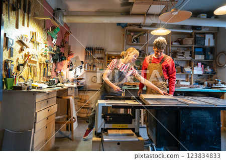 Enthusiastic couple of carpenters prepare stool base for saw machine in workshop. Apprentice teach 123834833
