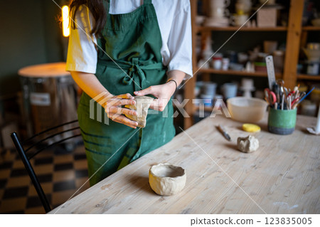 Woman potter hands shaping white clay bowl at wooden candle lit table in pottery workshop studio Woman potter hands shaping white clay bowl at wooden candle lit table in pottery workshop studio 123835005