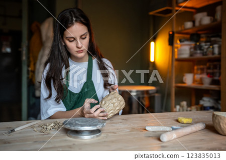 Molding craft ceramics: table in pottery studio with female artist shaping wet clay for potter bow 123835013