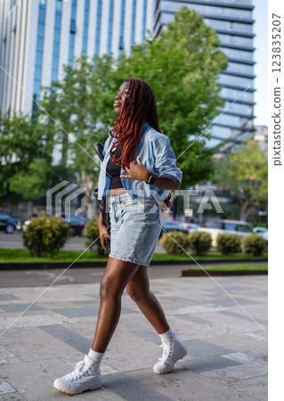Confident young African American woman walking down street in stylish denim outfit in city center 123835207