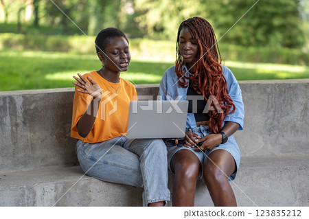 Two African American women on video call with laptop in park, studying and collaborating on project Two African American women on video call with laptop in park, studying and collaborating on project 123835212