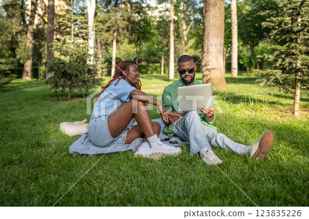 Calm African American couple sits under trees, studying online. Man browses exam resources on gadget Calm African American couple sits under trees, studying online. Man browses exam resources on gadget 123835226