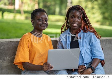 Smiling black women studying outdoors with laptop, remote work online research, exam preparation Smiling black women studying outdoors with laptop, remote work online research, exam preparation 123835303