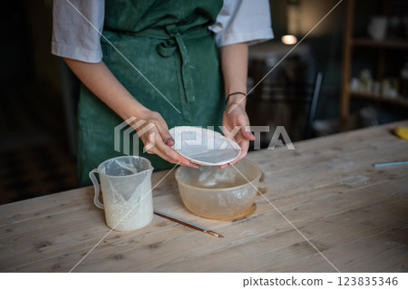 Potter hands glazing saucer on wooden table in workshop for ceramic durability and longevity 123835346