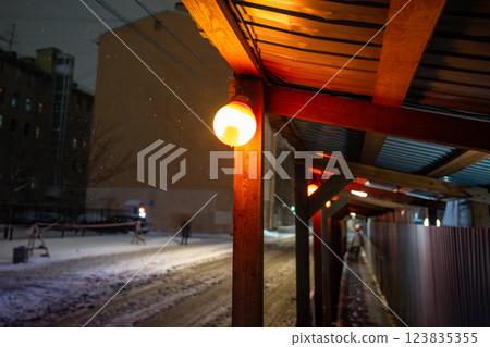 Snowstorm through construction site, canopy with lamps casting warm light on fall snow at night 123835355