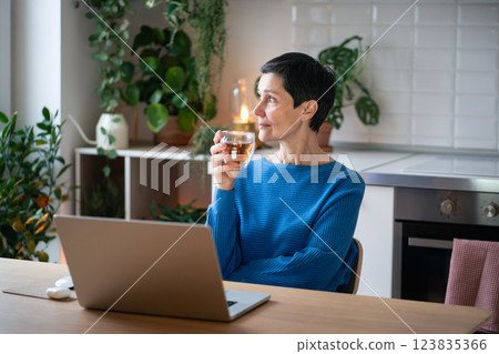 Calm thoughtful mature woman enjoying cup of tea during break from working remotely on laptop Calm thoughtful mature woman enjoying cup of tea during break from working remotely on laptop 123835366