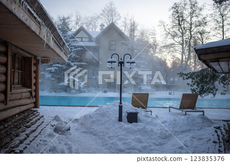 Open-air swimming pool with warm water, loungers and wooden Russian bath in sunny cold weather 123835376