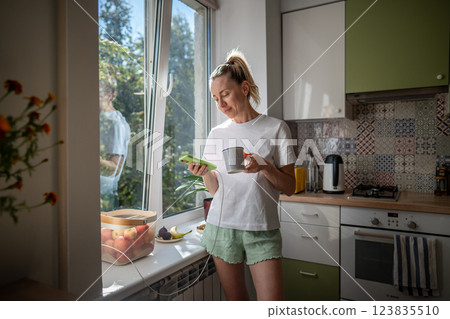 Calm smiling woman with coffee mug and phone in kitchen.Stress free lifestyle, morning rituals 123835510