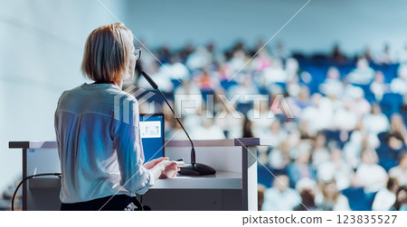Female speaker giving a talk on corporate business conference. Unrecognizable people in audience at conference hall. Business and Entrepreneurship event 123835527