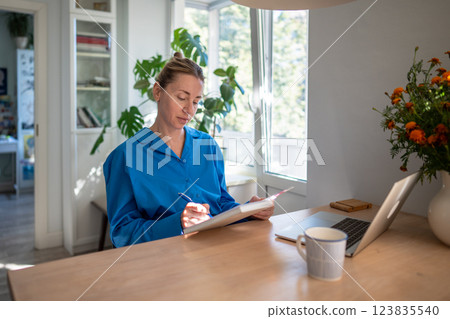 Focused on diary woman planning day in morning sitting at home with mug coffee, laptop writing notes 123835540