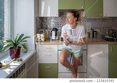 Happy woman enjoy coffee while looking out window in kitchen. No plans, simple living, mindfulness 123835545