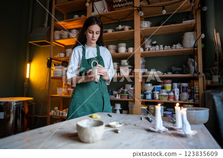 Female potter check molded clay mug for strength, touching handle in workshop. Craftsmanship skills Female potter check molded clay mug for strength, touching handle in workshop. Craftsmanship skills 123835609