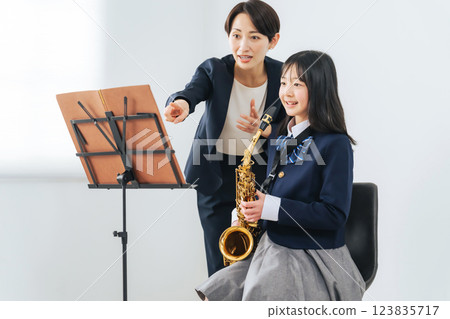 一位女老師指導女學生吹奏薩克斯風 一位女老師指導女學生吹奏薩克斯風 123835717