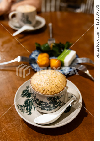 Traditional aromatic frothy coffee with milk served in retro cup and saucer paied with sweet kuih muih at kopitiam in Malaysia 123835839