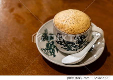 Traditional aromatic frothy coffee with milk served in retro cup and saucer at kopitiam in Malaysia Traditional aromatic frothy coffee with milk served in retro cup and saucer at kopitiam in Malaysia 123835840