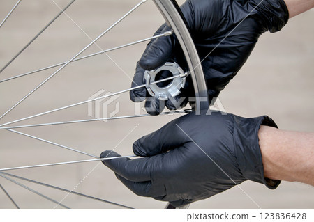Bicycle maintenance and repair. Hands in rubber gloves using a wrench adjust the tension of the spokes on the wheel 123836428