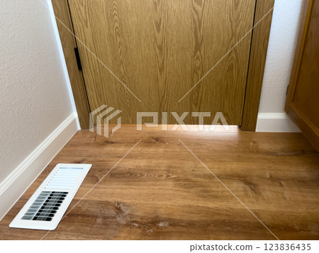 Bathroom Floor Vent with Wood Flooring. High quality photo A close-up of a white air vent installed on a wood-look bathroom floor. The vent is positioned near the baseboard, complementing the newly Bathroom Floor Vent with Wood Flooring. High quality photo A close-up of a white air vent installed on a wood-look bathroom floor. The vent is positioned near the baseboard, complementing the newly 123836435