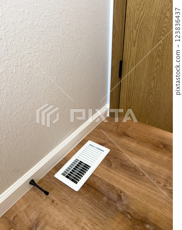 Bathroom Floor Vent with Wood Flooring. High quality photo A close-up of a white air vent installed on a wood-look bathroom floor. The vent is positioned near the baseboard, complementing the newly Bathroom Floor Vent with Wood Flooring. High quality photo A close-up of a white air vent installed on a wood-look bathroom floor. The vent is positioned near the baseboard, complementing the newly 123836437