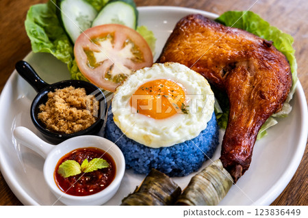 Closeup of nasi kerabu, popular delicacy in Malaysia with rice dyed in blue color, served with fried chicken, eggs, kerisik, vergetable and sauces Closeup of nasi kerabu, popular delicacy in Malaysia with rice dyed in blue color, served with fried chicken, eggs, kerisik, vergetable and sauces 123836449