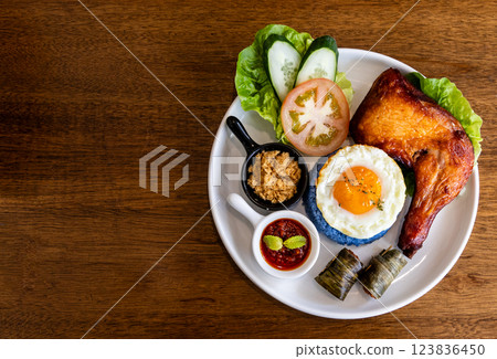 Overhed view of nasi kerabu, popular delicacy in Malaysia with rice dyed in blue color, served with fried chicken, eggs, kerisik, vergetable and sauces 123836450