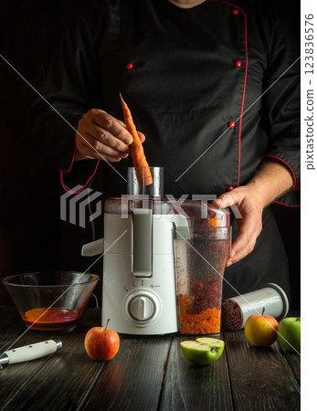 A chef prepares juice from fresh vegetables and fruits on a kitchen table. The chef fills a juicer with chopped carrots. A chef prepares juice from fresh vegetables and fruits on a kitchen table. The chef fills a juicer with chopped carrots. 123836576