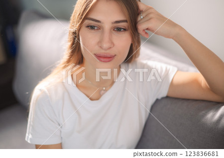 Young woman frustrated in a white T-shirt, sitting on sofa in modern living room during daytime thoughtful emotions 123836681
