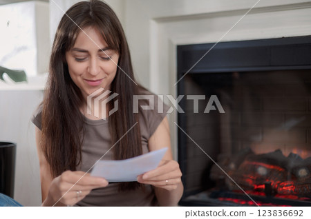 Young lady is seated at a kitchen table, attentively using a pen to write on a piece of paper writes a letter 123836692
