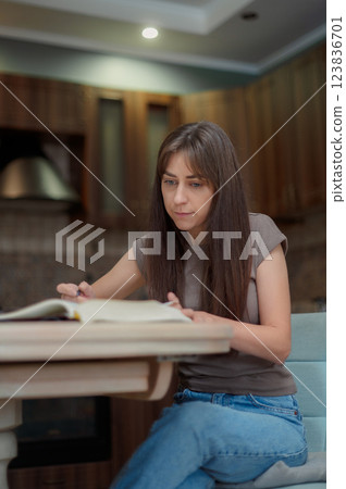 Female student learning and preparing exam at home. Woman reading textbook and taking notes 123836701