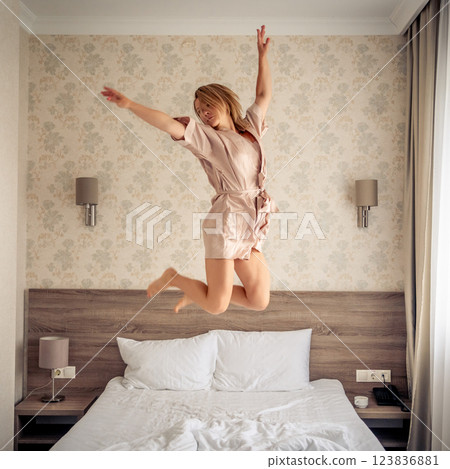 Woman having fun and jumping with bathrobe on bed in hotel room Woman having fun and jumping with bathrobe on bed in hotel room 123836881