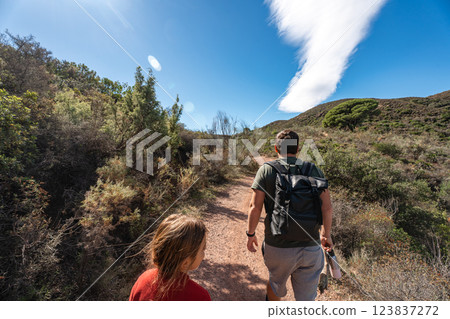 Young adults hiking in nature trail under blue sky with cloud formation Young adults hiking in nature trail under blue sky with cloud formation 123837272