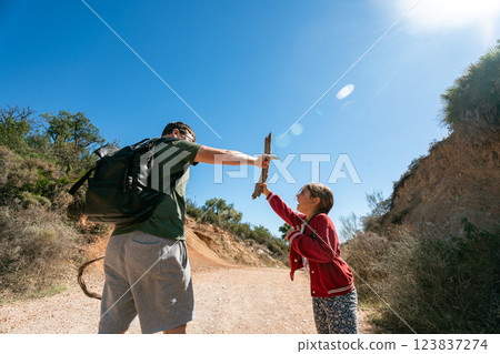 Caucasian male adult and young girl playing with sticks on sunny nature trail Caucasian male adult and young girl playing with sticks on sunny nature trail 123837274
