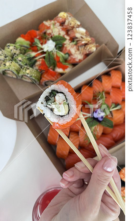 Sushi in hand on the background of a box with various sushi. Chopsticks for sushi. Sushi delivery. Lifestyle. Sushi in hand on the background of a box with various sushi. Chopsticks for sushi. Sushi delivery. Lifestyle. 123837458